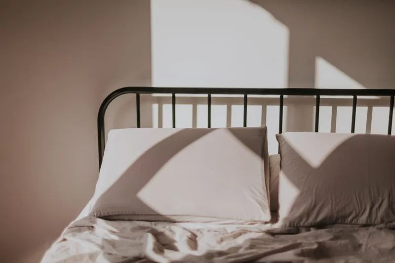 unmade bed in morning light, plain cotton bedding