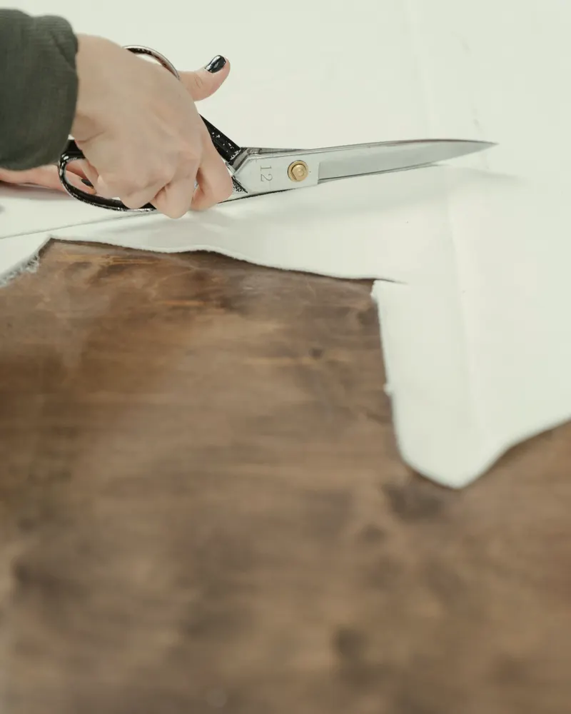 a hand cutting a length of cotton with tailor's shears on a dark wood table